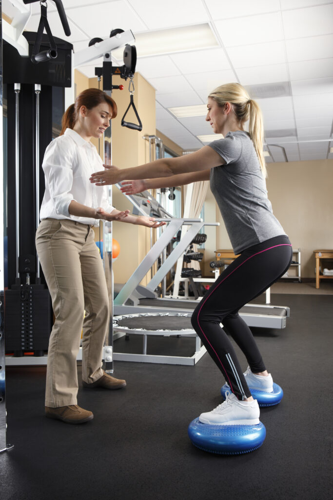 A physical therapist working with  young female patient on a pair of balance discs in a physical therapy clinic.